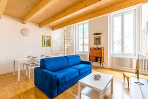 A living room with a blue sofa, white coffee table, and a white dining table with chairs. There is a spiral staircase leading to an upper level. - Nova Stylish House in center (Naples)