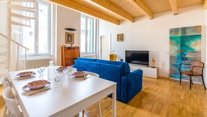Un salon moderne avec une table blanche dressée pour le repas, un canapé bleu, un téléviseur et un tableau accroché au mur.