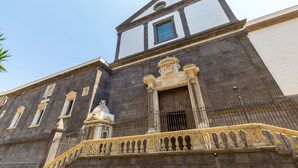 Un bâtiment historique doté d’un imposant clocher, d’un balcon orné de balustrades travaillées et d’une grande fenêtre avec des vitres teintées de bleu.