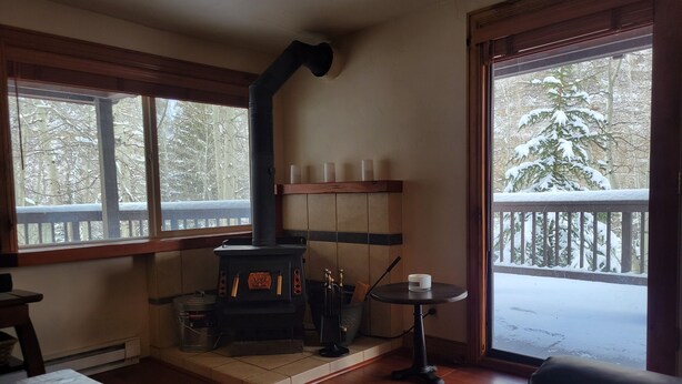 A cozy room with a wood-burning stove, a dining table, and a view of a snowy deck.