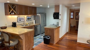 A modern kitchen with wooden cabinets, a stainless steel refrigerator, a coffee maker, and a bar area with stools.