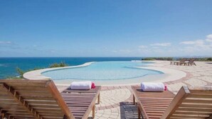 A pool with a curved edge, surrounded by lounge chairs and a paved deck. - Luna Sul Mare - 2 Bed 2.5 Bath Condo with gorgeous ocean view! (Sint Maarten)