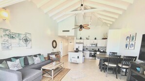 A spacious living area with a sofa, coffee table, and dining set. A kitchen is visible in the background with modern appliances. - Luna Sul Mare - 2 Bed 2.5 Bath Condo with gorgeous ocean view! (Sint Maarten)