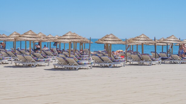 Une plage bordée de rangées de chaises longues et d’ombrelles en chaume.