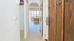 Un couloir menant à une chambre dotée d’une grande porte en bois, de murs blancs et d’un sol carrelé.