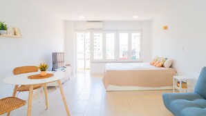 Une pièce lumineuse et moderne, comprenant un lit, un canapé bleu, une table à manger avec des chaises et un téléviseur.