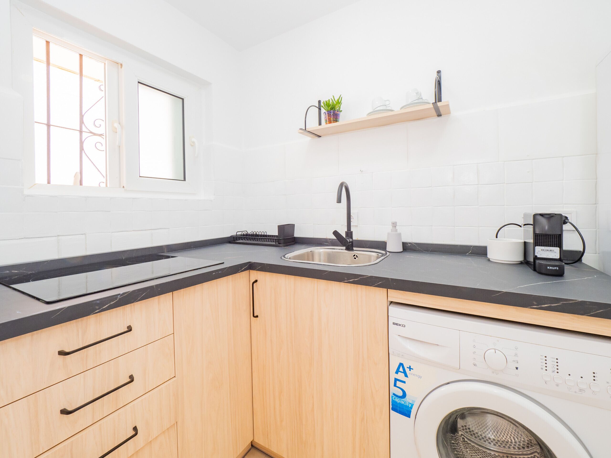 Una cocina moderna con lavadora integrada, un lavamanos y un ventanal con barandillas decorativas.