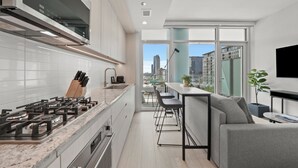 A modern kitchen with a gas stove, white cabinets, and a view of the city through large windows. - Level Chicago Fulton Market (Chicago)