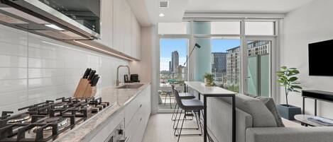 A modern kitchen with a gas stove, white cabinets, and a view of the city through large windows.