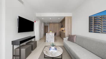 En moderne stue med et fladskærms-tv, et marmorbord, en grå sofa og et køkken i baggrunden.