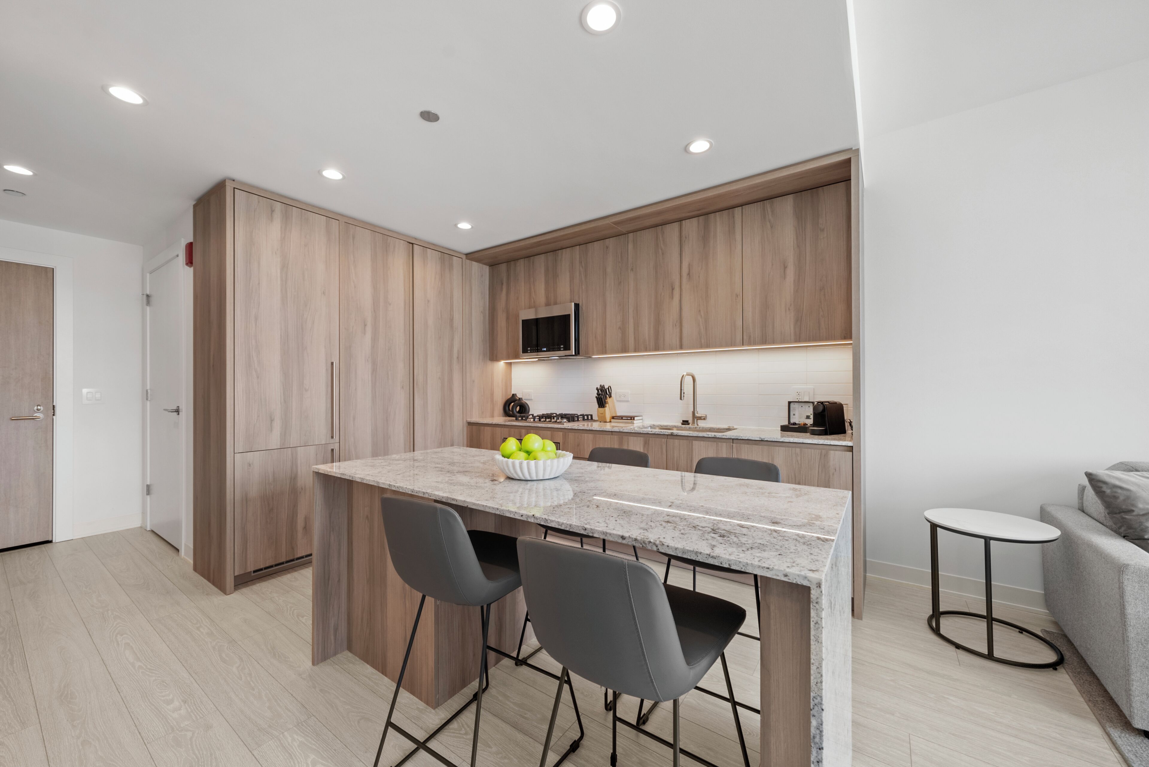 A modern kitchen with wooden cabinets, a marble countertop, and a built-in microwave.