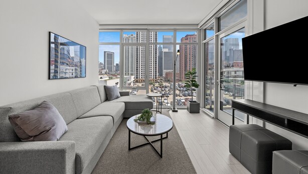 A modern living room with a grey sofa, a round coffee table with a plant, and a TV mounted on the wall. - Level Chicago Fulton Market (Chicago)