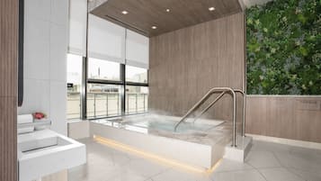 Uma casa de banho moderna com hidromassagem envidraçada, parede de madeira com jardim vertical e vista para a cidade através de grandes janelas.