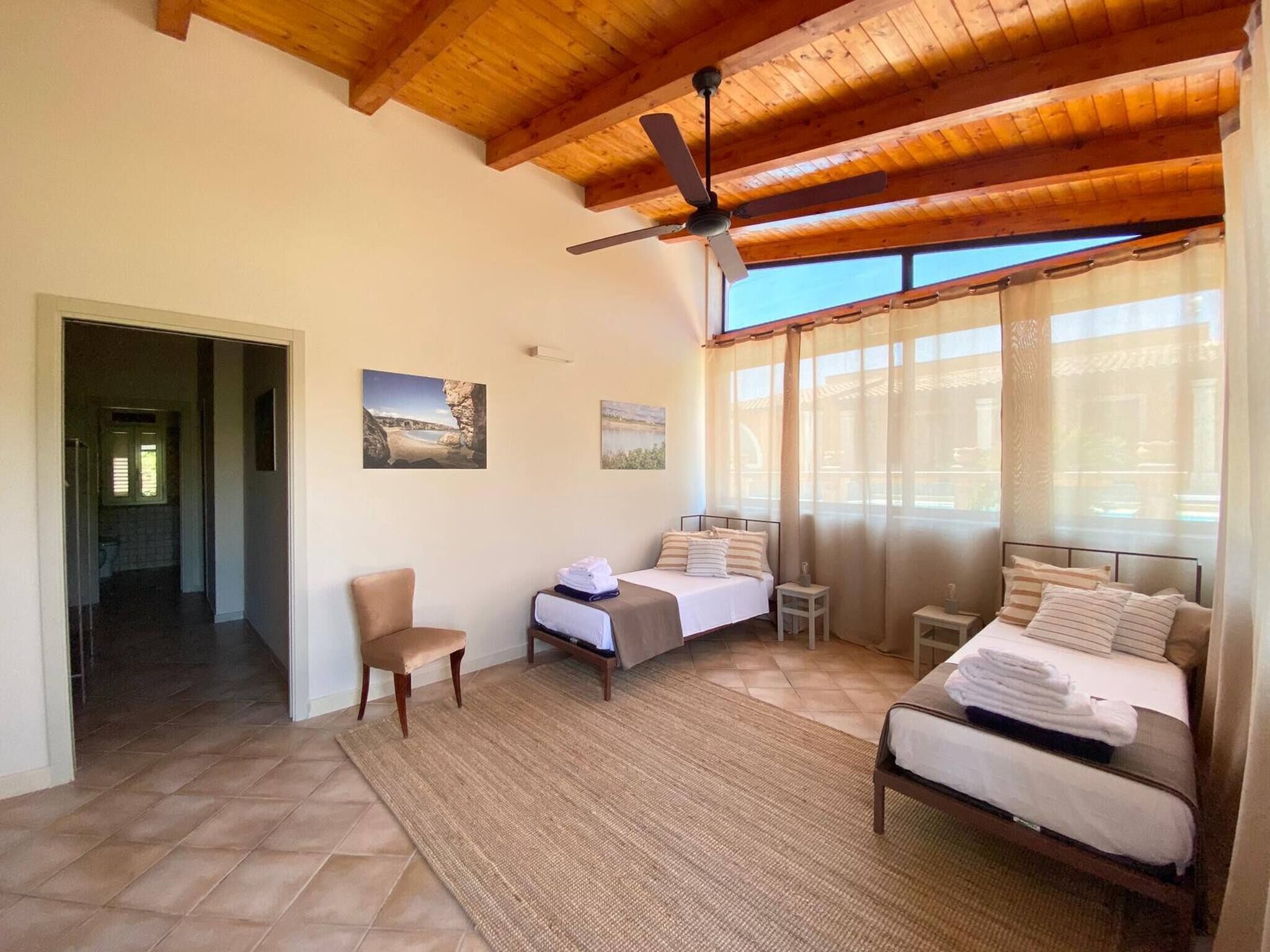 A bedroom with two beds, a ceiling fan, and a view of the outdoors.
