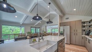 Une cuisine spacieuse dotée d’un grand îlot central, d’un éclairage moderne suspendu et offrant une vue sur l’extérieur.