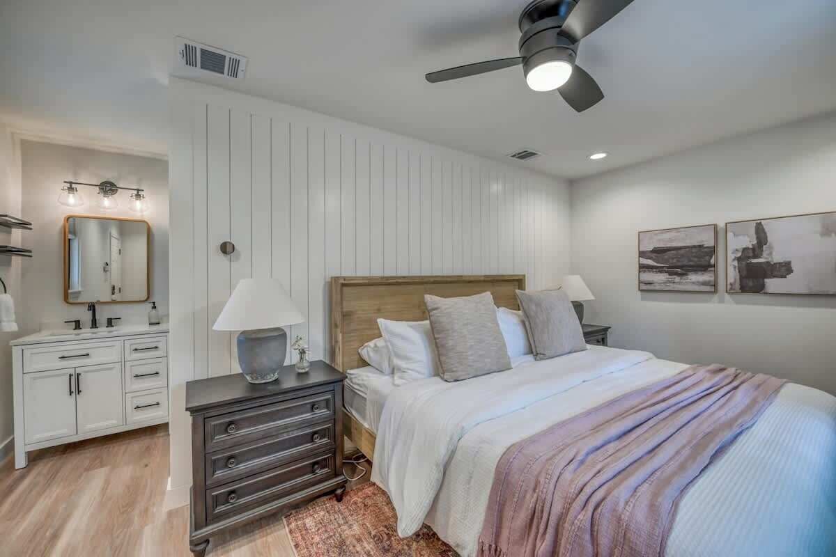 A bedroom with a bed, bedside tables, a dresser, a ceiling fan, and wall-mounted artwork.