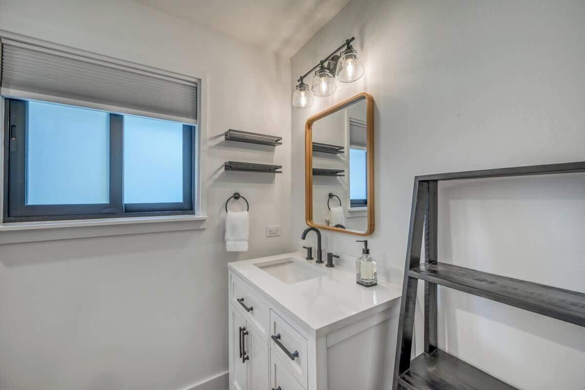A bathroom with a white vanity, a mirror with a wooden frame, and a window with blinds.