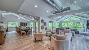 Un salon spacieux avec un haut plafond, de grandes fenêtres et un coin repas doté de meubles en bois.