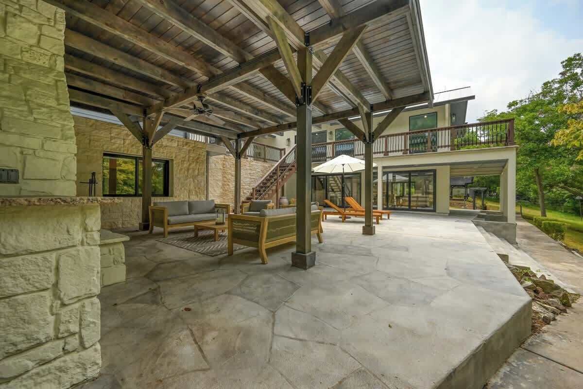 A covered patio area with stone flooring, wooden furniture, and a view of the house's exterior.