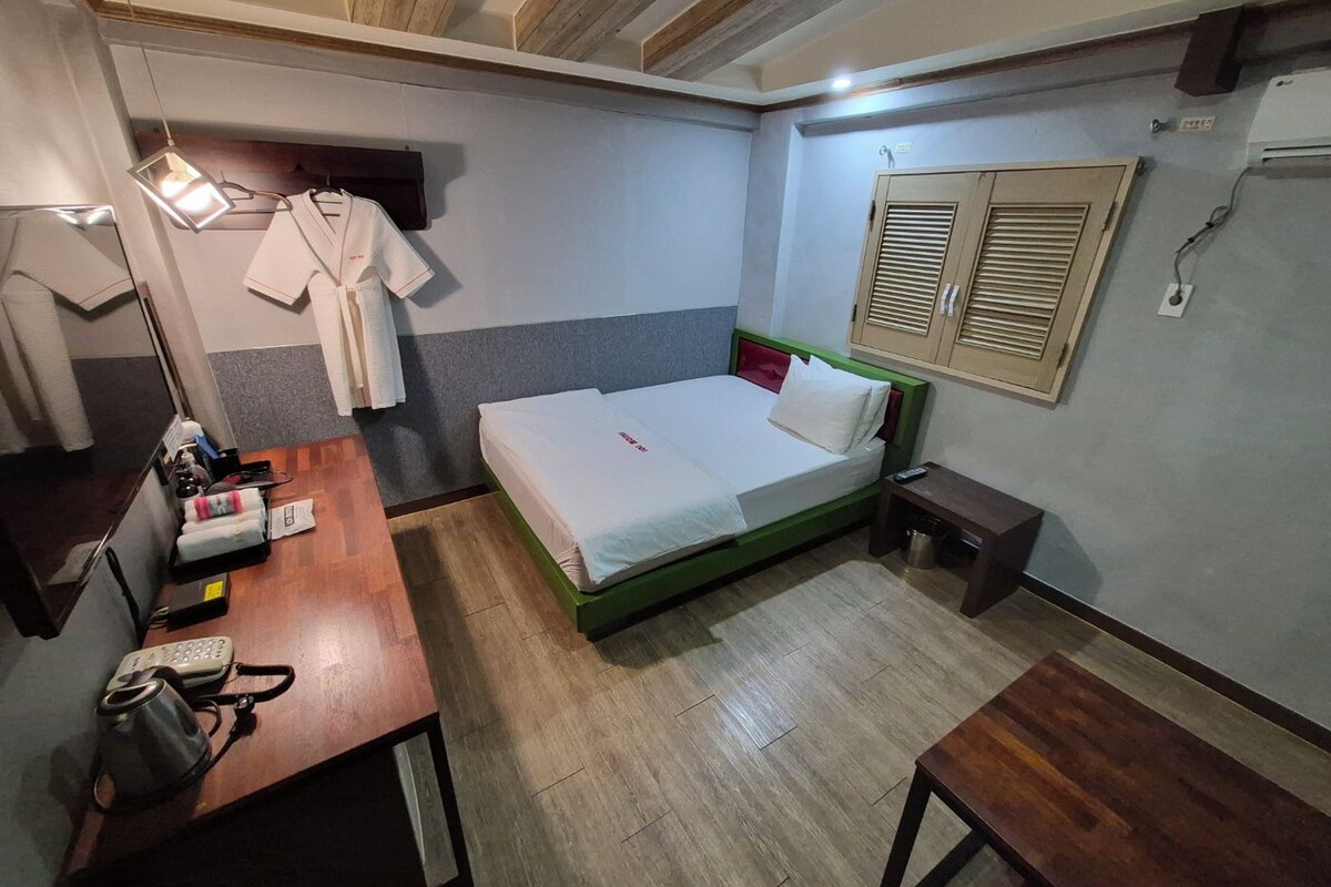 A hotel room with a bed, bedside table, and a desk with a telephone and a kettle.