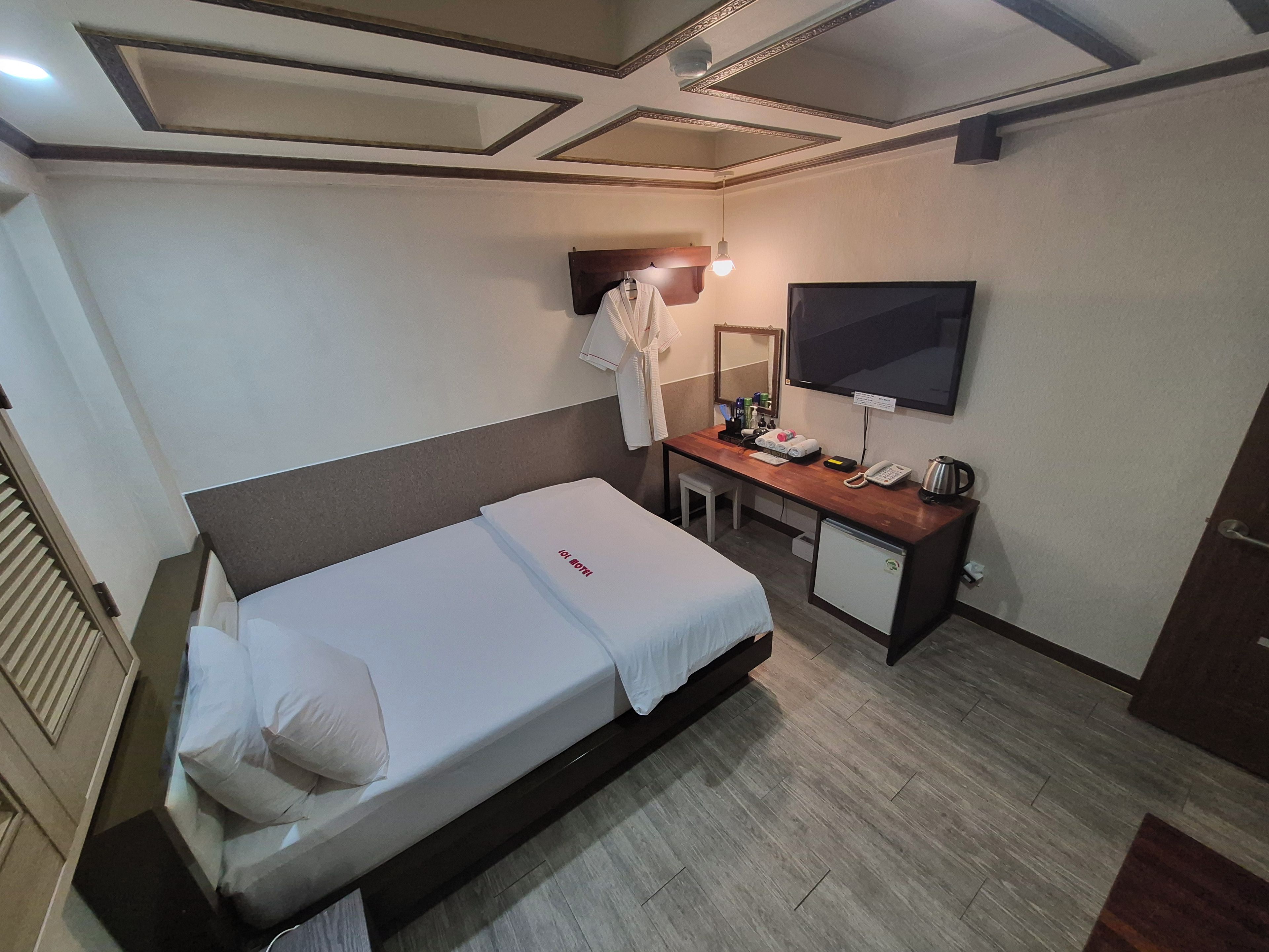 A hotel room with a bed, a desk, a mirror, a television, and a small refrigerator.