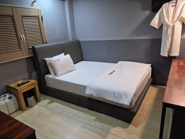 A single bed with a grey headboard, a bedside table with a remote control, and a small trash bin. - LOL Motel (Daegu)