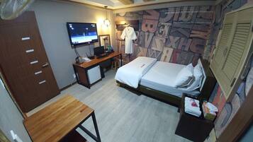 A hotel room with a bed, a desk, a TV, and a wall with letters.