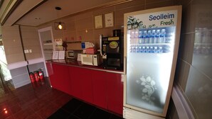 A hotel reception area with a red counter, a Seolleim Fresh water dispenser, a coffee machine, and a fire extinguisher.