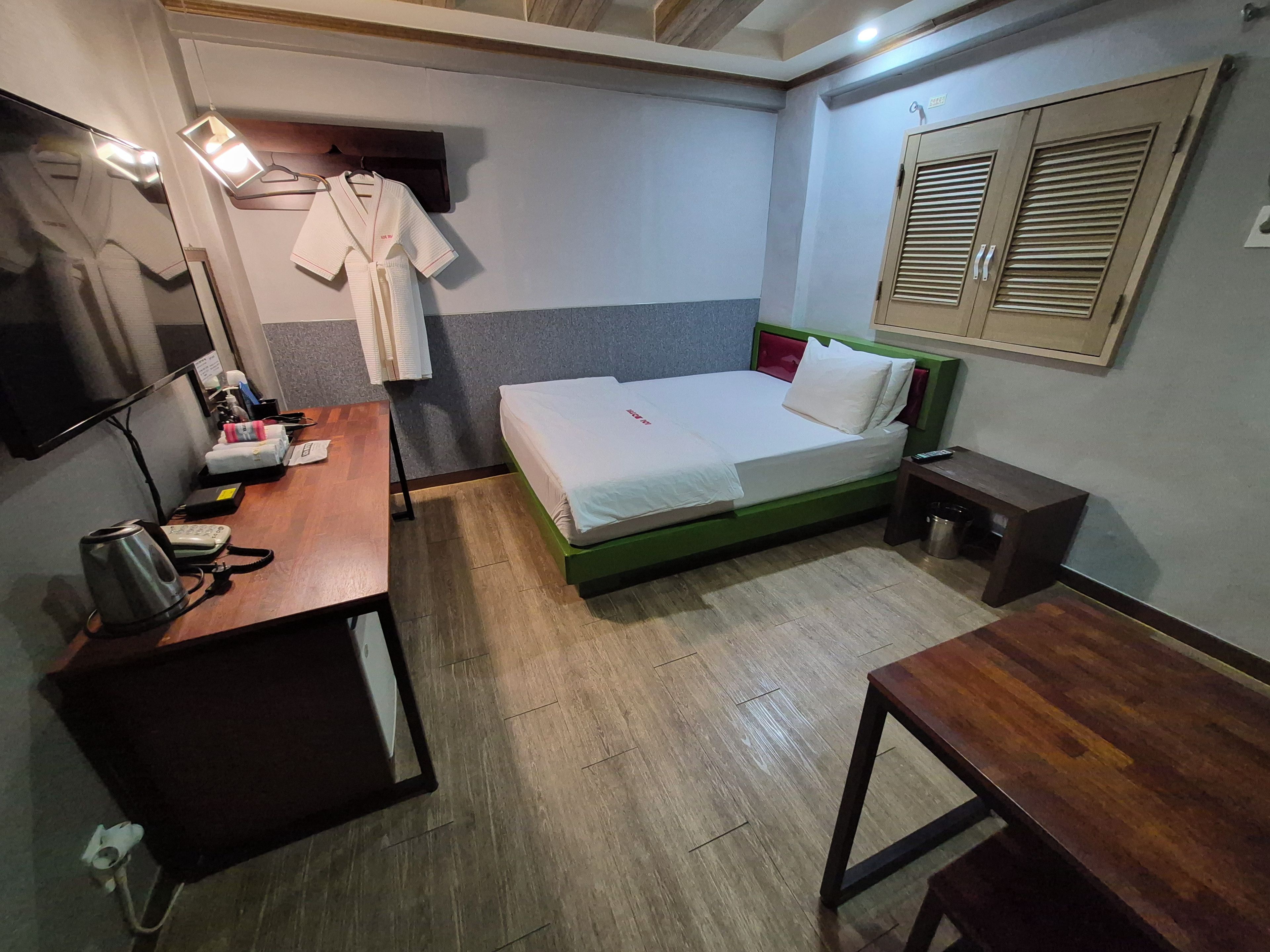 A hotel room with a bed, a desk, a chair, a TV, and a wardrobe.