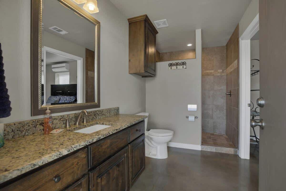 A bathroom with a granite countertop, wooden cabinets, a white toilet, and a shower area with stone tiles.