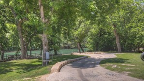 A paved pathway curving through a park with trees and a body of water in the background. - Let's Go Tubing! Awesome House-next to River! (New Braunfels)