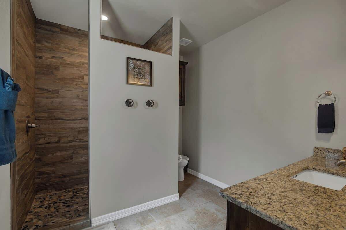 A bathroom with a wooden shower enclosure, a sink with a granite countertop, and a toilet.