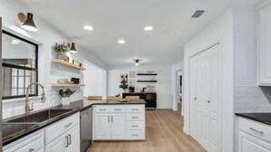 A modern kitchen with white cabinetry, a central island, and built-in shelves. - Bubbles on Bowie Walk to Main St (Fredericksburg)