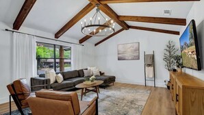A modern living room with a wooden ceiling, a large window, a sofa set, a coffee table, and a TV. - Bubbles on Bowie Walk to Main St (Fredericksburg)