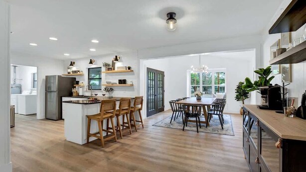A spacious kitchen with wooden flooring, a central island with bar stools, and a dining area with a large table and chairs. - Bubbles on Bowie Walk to Main St (Fredericksburg)