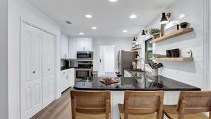 A modern kitchen with white cabinetry, a black countertop island, and two wicker chairs. - Bubbles on Bowie Walk to Main St (Fredericksburg)