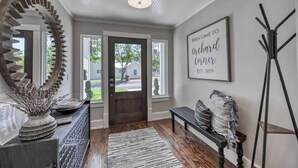 A hallway with a large mirror, a welcome sign, a bench, and a coat rack.