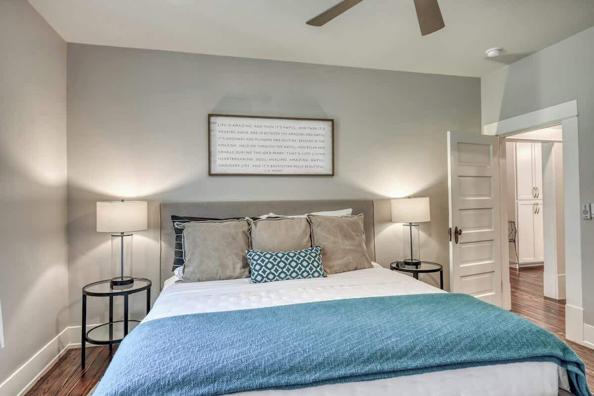 A bedroom with a bed, two bedside tables, a ceiling fan, and a framed quote on the wall.