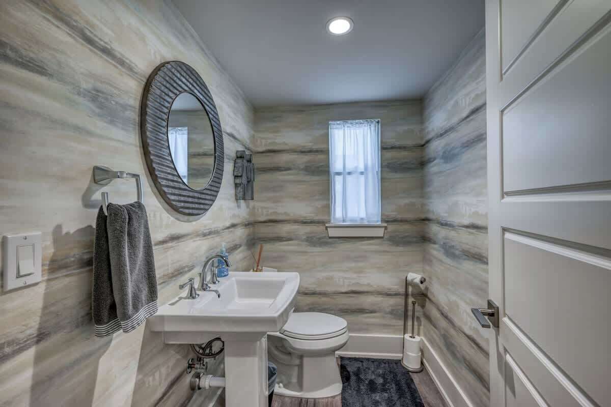 A bathroom with a marble wall, a sink, a toilet, a mirror, and a window.