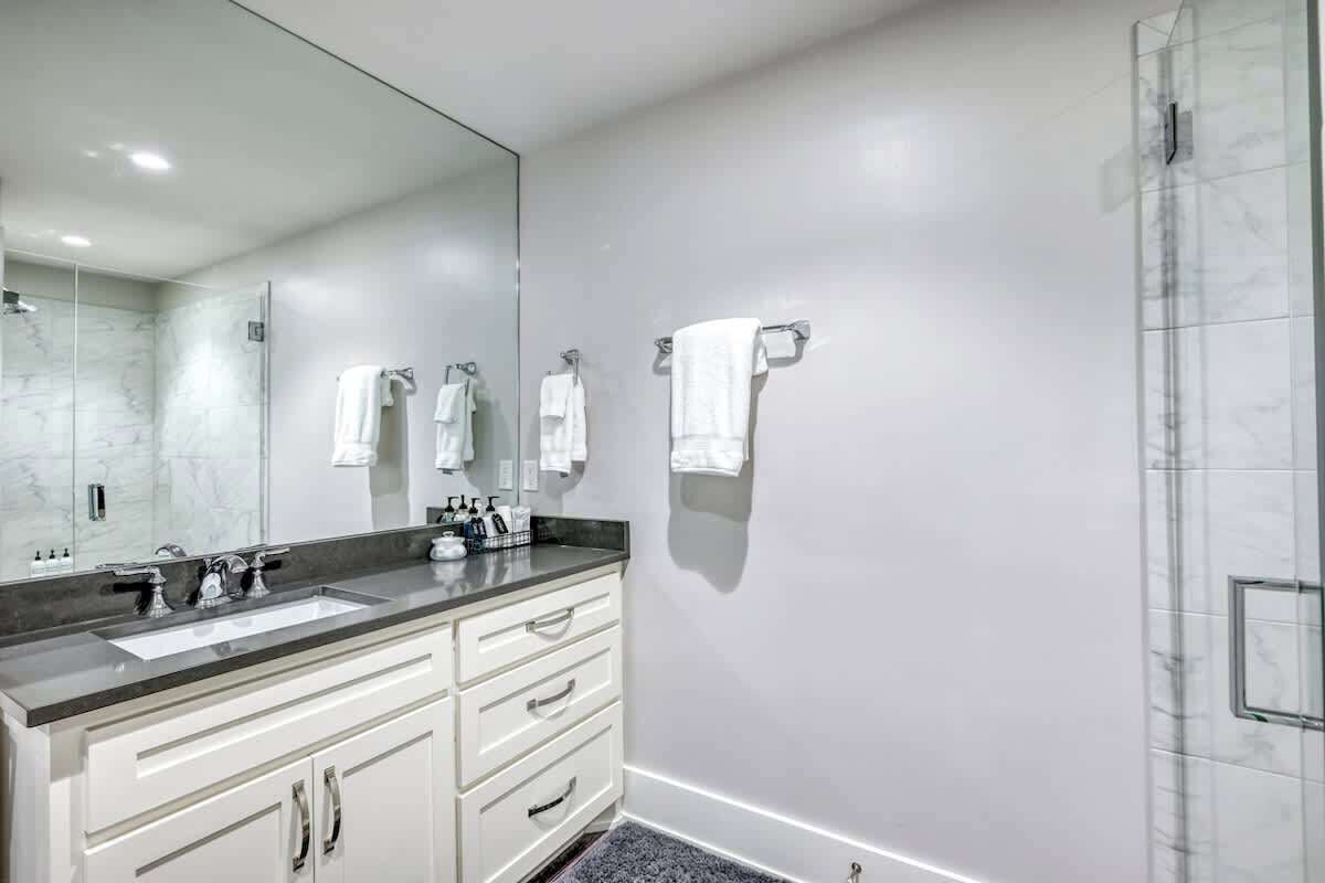 A modern bathroom with a large mirror, a sink, and a shower.