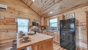 Une cuisine rustique, située dans une cabane en bois, avec un îlot central, un réfrigérateur noir et des armoires en bois.
