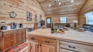 L’intérieur d’une cabane en bois comprend un coin cuisine, des placards en bois, une table à manger avec des chaises et un ventilateur de plafond.