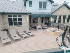 A patio with lounge chairs, a hot tub, and a stone building with a metal roof. - Spicewood Lodge With Pool, Hot Tub (Spicewood)
