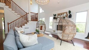 Un salon spacieux avec un canapé gris, des fauteuils en osier, un escalier et une cheminée.