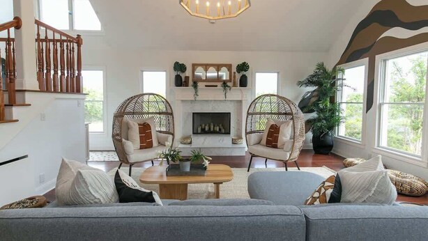 Un salon spacieux avec une cheminée, deux fauteuils en osier, un canapé et un escalier.
