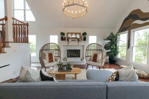 Amplia sala de estar con chimenea, dos sillones de mimbre, un sofá y una escalera.