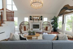 Amplia sala de estar con chimenea, dos sillones de mimbre, un sofá y una escalera.