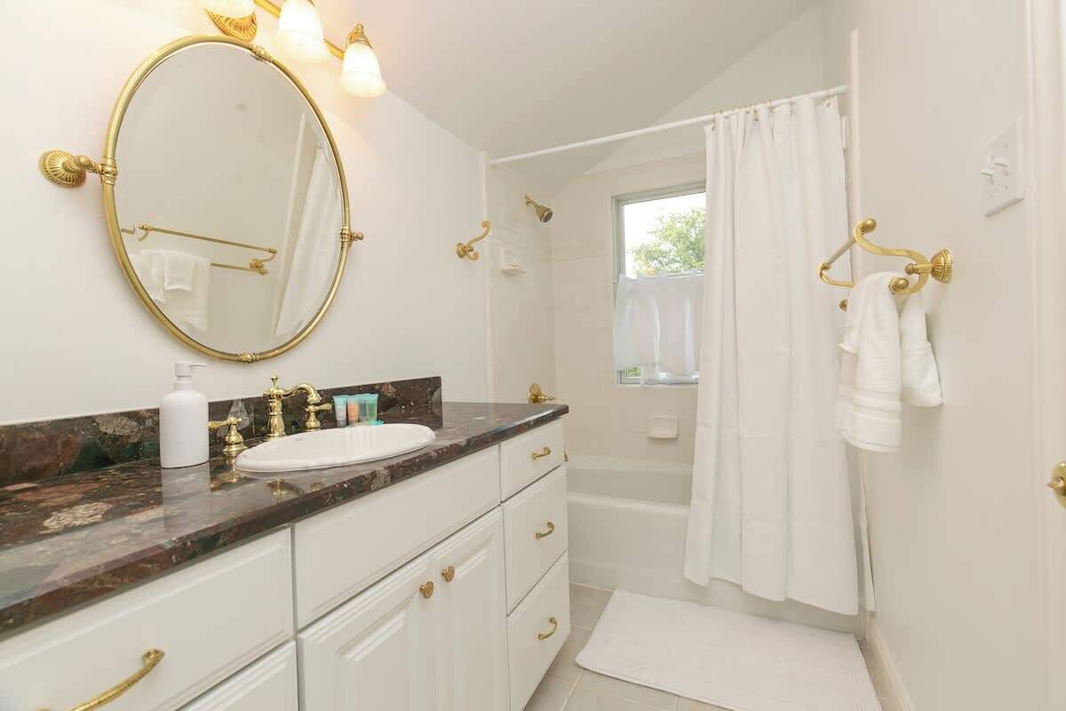 A bathroom with a marble countertop, gold fixtures, a large mirror, a bathtub, and a shower curtain.