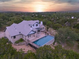 Una casa grande con piscina, rodeada de árboles y un paisaje montañoso.