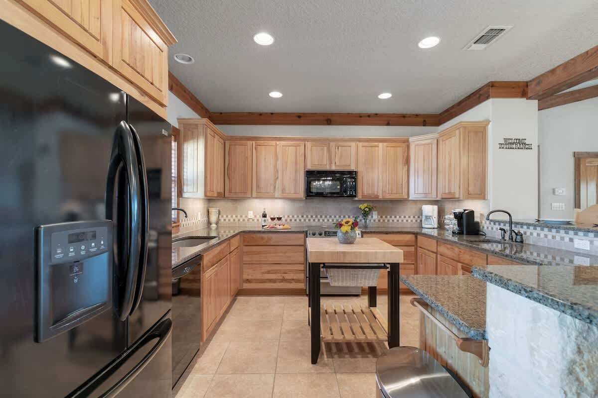 A modern kitchen with wooden cabinets, a stainless steel refrigerator, a microwave, and a granite countertop.
